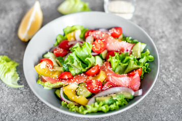 Salted salmon salad with fresh green lettuce, cucumbers, tomatoes, sweet peppers and red onions on a stone background. Ketogenic, keto or paleo diet lunch bowl.