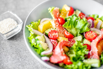 Salted salmon salad with fresh green lettuce, cucumbers, tomatoes, sweet peppers and red onions on a stone background. Ketogenic, keto or paleo diet lunch bowl.