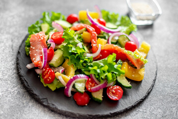 Salted salmon salad with fresh green lettuce, cucumbers, tomatoes, sweet peppers and red onions on a stone background. Ketogenic, keto or paleo diet lunch bowl.