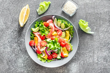 Salted salmon salad with fresh green lettuce, cucumbers, tomatoes, sweet peppers and red onions on a stone background. Ketogenic, keto or paleo diet lunch bowl.