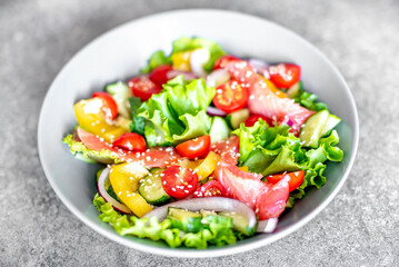 Salted salmon salad with fresh green lettuce, cucumbers, tomatoes, sweet peppers and red onions on a stone background. Ketogenic, keto or paleo diet lunch bowl.