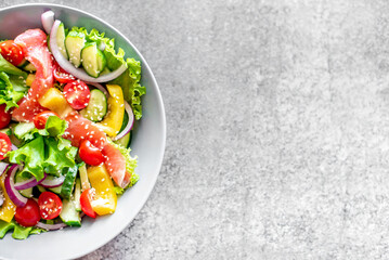 Salted salmon salad with fresh green lettuce, cucumbers, tomatoes, sweet peppers and red onions on a stone background with copy space for your text. Ketogenic, keto or paleo diet lunch bowl.