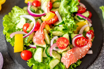 Salted salmon salad with fresh green lettuce, cucumbers, tomatoes, sweet peppers and red onions on a stone background 