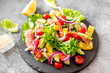 Salted salmon salad with fresh green lettuce, cucumbers, tomatoes, sweet peppers and red onions on a stone background 