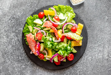 Salted salmon salad with fresh green lettuce, cucumbers, tomatoes, sweet peppers and red onions on a stone background 