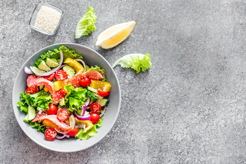Salted salmon salad with fresh green lettuce, cucumbers, tomatoes, sweet peppers and red onions on a stone background with copy space for your text. Ketogenic, keto or paleo diet lunch bowl.