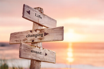 life changing event text quote on wooden crossroad signpost outdoors on beach with pink pastel...