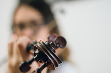 close up of violin scroll and pegs with blurred woman playing in background and copy space. © SETO fotografias