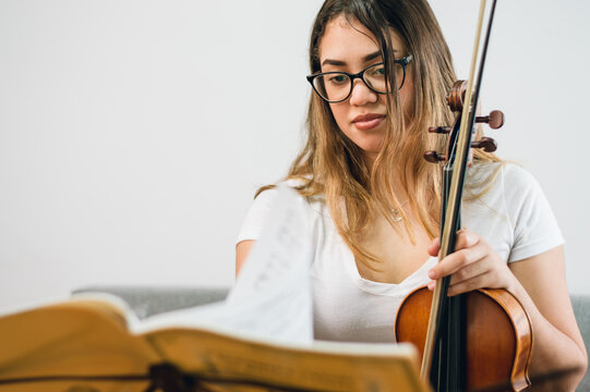 young latin woman violinist at home studying sheet music sitting with the violin in her hand
