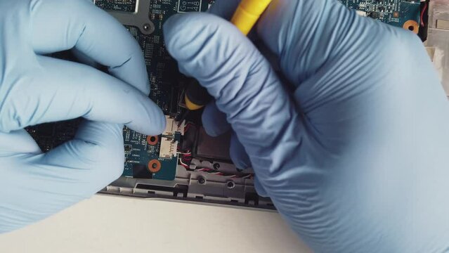 Man wearing gloves removing internal connections from a laptop with the help of a screwdriver