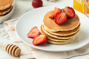 American pancakes decorated with strawberries and sprinkled with powdered sugar in a white plate. Healthy and tasty breakfast