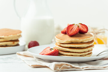 American pancakes stacked in a pile decorated with strawberries in a white plate. Healthy and tasty breakfast
