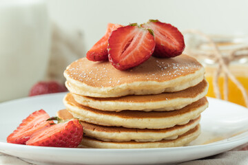 American pancakes decorated with strawberries and sprinkled with powdered sugar in a white plate. Healthy and tasty breakfast