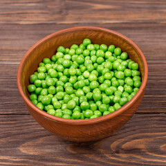 Fresh green peas in a bowl close-up on a brown wooden table.