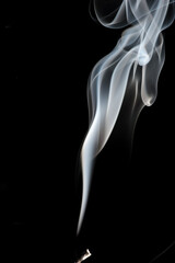 Puffs and curls of white smoke against a black background rising from a burning stick
