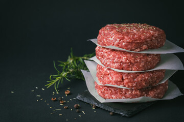 Raw ground beef burger patties separated by baking paper on a black background - obrazy, fototapety, plakaty