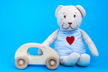 Baby wooden car toy and toy bear witn heart embroidered in striped clothes on blue background. Concept of baby toys. 