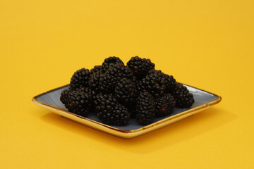 Blackberries in a plate on a yellow background. Close-up
