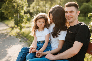 Fototapeta premium Young family dad mom and daughter enjoy a warm evening in the park