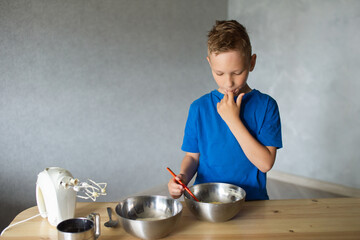 A child prepares dough in metal bowls. Trying the dough