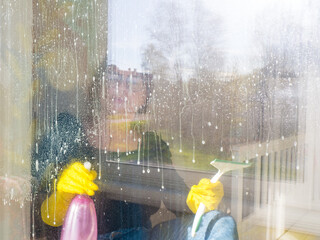 a girl's hand in a glove washes the windows with a spray detergent. housework concept.