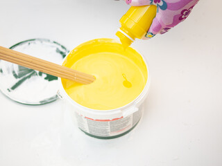 Obraz na płótnie Canvas girl painter mixes yellow and white paints, mixes colors with acrylic facade paint. paint mixes in bucket