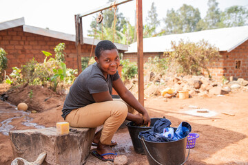 Young african girl washes clothes outside with laundry soap and a bucket.