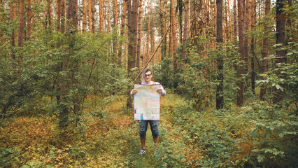 Obraz premium Traveling man with dreadlocks with map in woods. Male traveler with backpack in woods reading map in cloudy weather