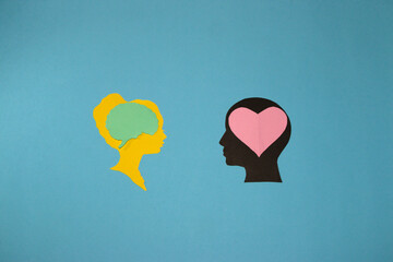 male and female paper head looking at each other man in love has a heart brain female head is not and has a brain, creative art design on a pastel blue background
