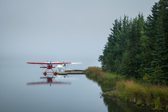 Two Alaskan red and white float airplanes on edge of river 