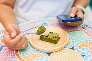Closeup woman is eating Matcha green tea cake while using the smartphone in the cafe