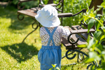 baby girl have fun outdoor, sunny day, toddler in garden holding hand on antique chair, view from behind - obrazy, fototapety, plakaty