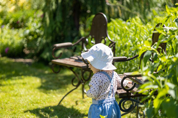 baby girl have fun outdoor, sunny day, toddler in garden holding hand on antique chair