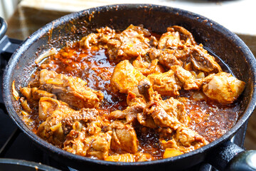 Fried chicken in spices and sauce is hot in a frying pan.