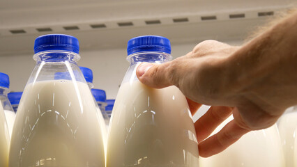 Close-up of many plastic milk bottles with blue caps and a male buyer's hand takes one