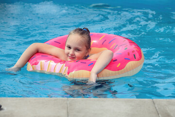 an eight-year-old girl has fun and actively spends her holidays in an outdoor pool in cool water in the summer, she is wearing a bright red inflatable ring