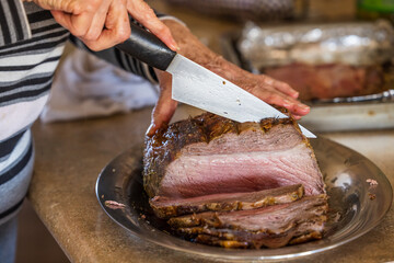 A woman slicing a large prime rib beef roast that was baked and roasted in the oven by a home gourmet chef for a holiday Christmas dinner
