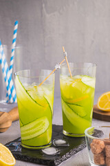 Refreshing drink, cucumber lemonade with ice and slices of fresh cucumber in tall glasses on a gray concrete background. Recipes for non-alcoholic soft drinks