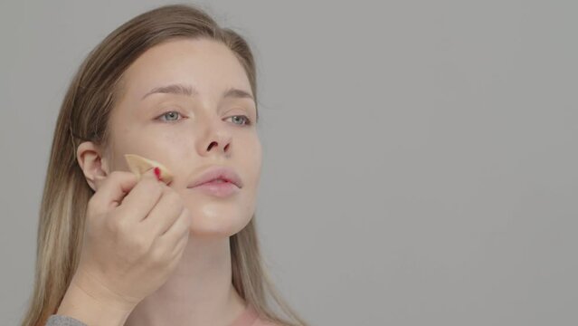 Makeup artist or stylist applies foundation using wet sponge to the face of the female model. Visagiste  applying cosmetic concealer base on a face. Professional makeup. Tutorial makeup master class