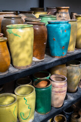 Many unique handmade colorful clay jugs and vases of various shapes on shelf in local market. Lot of handicraft ceramic pots. 