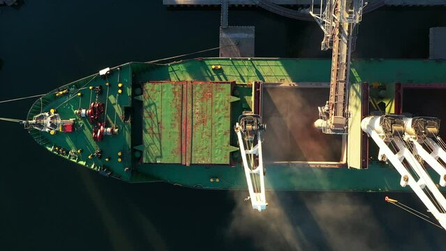Aerial view fom above - wheat loading to bulker ship cargo hold at sea grain elevator in sea port. Wheat shipment from silo to vessel via moving trunk at a sea port terminal. Maritime transport.