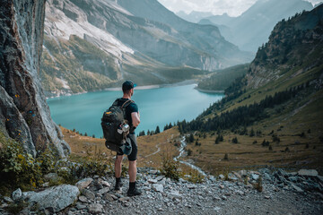 Un homme randonneur qui est en montagne lors d'une randonnée et qui regarde le magnifique panorama, avec un lac, des chemins et une forêt.