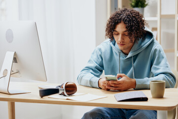 guy with curly hair in a blue jacket in front of a computer with phone Lifestyle