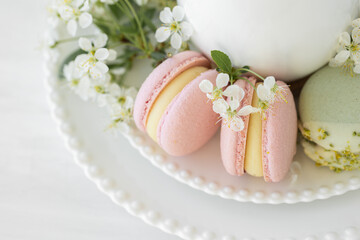 Fototapeta na wymiar Traditional delicious French dessert - sweet homemade macarons on a vintage plate. Colourful tasty macaroons served on a white china with herbal tea. Decorated with fragile cherry tree flowers. 