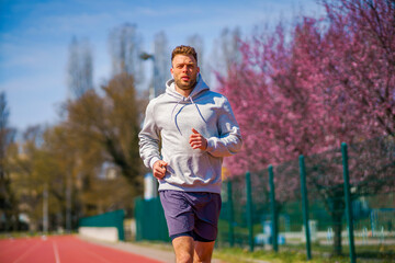 A man in a gray hoodie is jogging at a sports stadium.