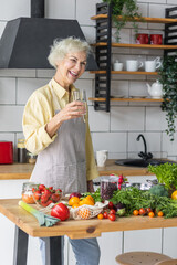 Senior woman pensioner with a glass of clean water in her kitchen. Concept of healthy eating for mature female, vegetarian diet, detox, vitamin salad. Health care and healthy lifestyle