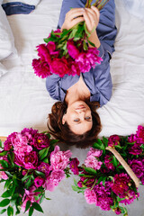 happy morning. a woman in pajamas in bed with a peonies.