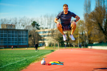 A handsome young man jumps high in the open at a sports stadium.