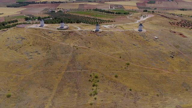 Windmills of Alcazar de San Juan perspective from drone. Beautiful and unique agriculture landscape with four windmills on top of the hills. Drone backward and tilt up Beautiful colours of agriculture