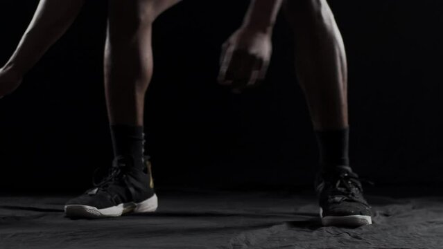 Basketball player bouncing a ball. African american sports man practicing against black background..